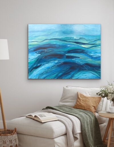 En hyggekrog med et stort maleri i blå og grønne nuancer på væggen ved en daybed med sidebord og lampe.